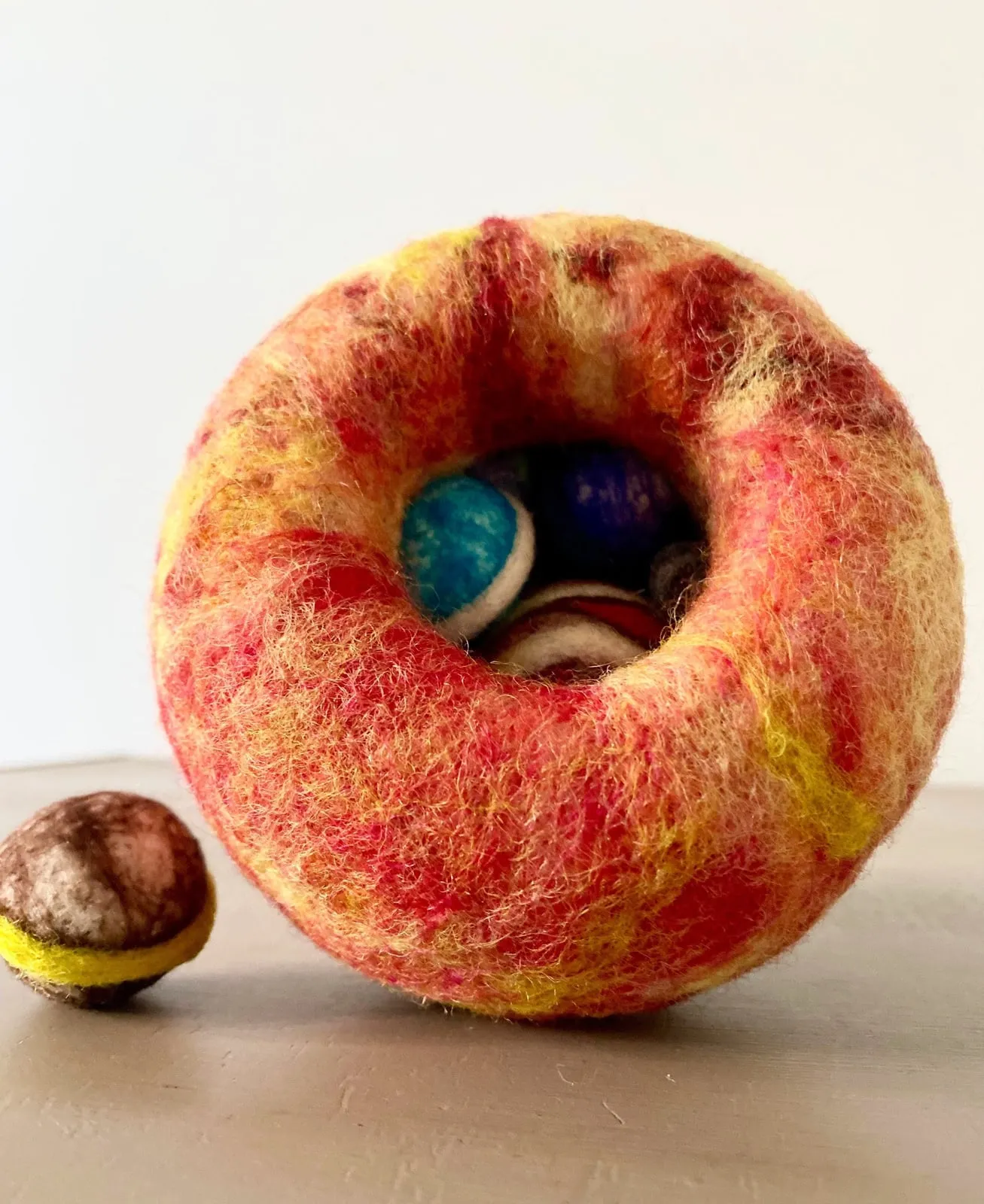 A large orange needle-felted planet holding a nested set of smaller felted planets